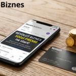 Zdjęcie bliskiego planu nowoczesnego smartfona na drewnianym biurku, wyświetlającego przejrzystą aplikację bankowości mobilnej z napisem w języku polskim: "REVOLUT BIZNES i 500zł PREMII". Obok telefonu leży elegancka, metalowa karta biznesowa i stos złotych monet.