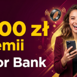 Reklama Alior Banku z ofertą 'Do 1300 zł premii'. Na obrazku uśmiechnięta kobieta ze smartfonem i zaciśniętą pięścią, obok której unosi się inteligentny pierścień płatniczy. Tło jest bordowo-złote.
